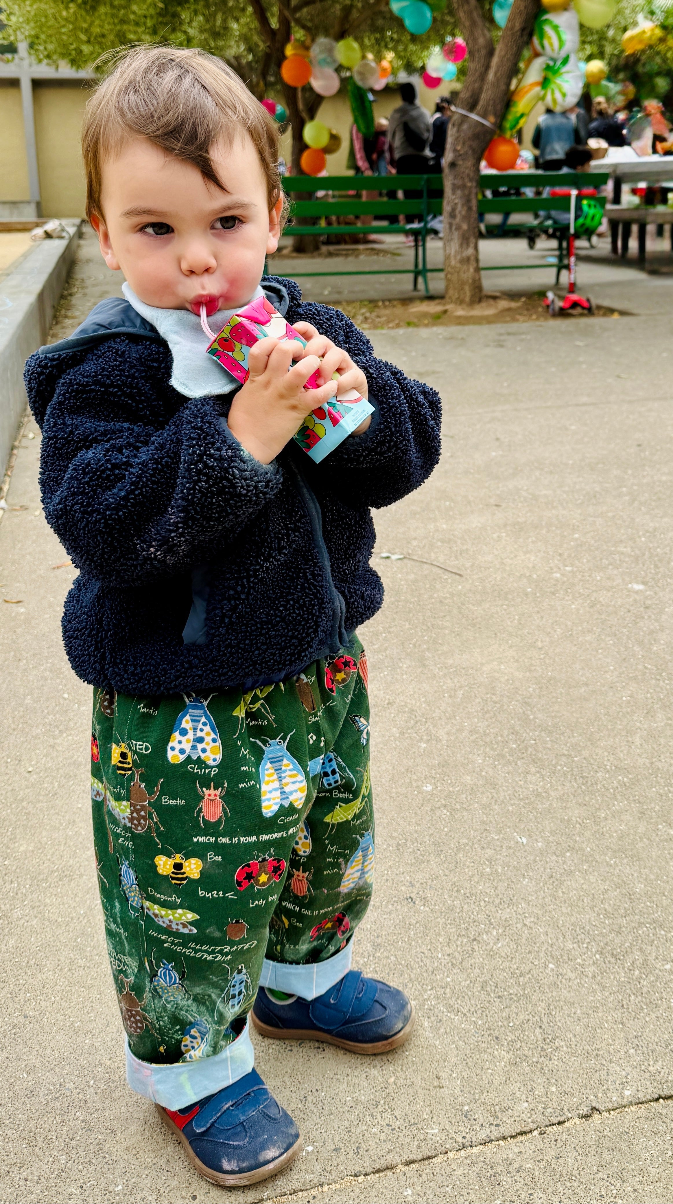 Child in outdoor setting with colorful balloons and people in the background